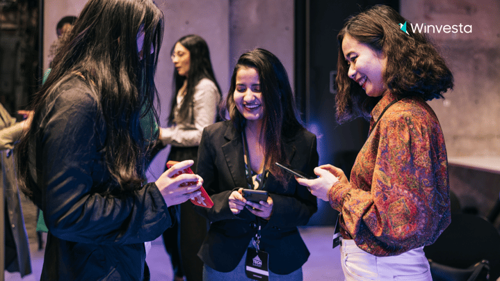 A group of young professionals networking at a tech event, smiling and engaging in conversation while using their smartphones.